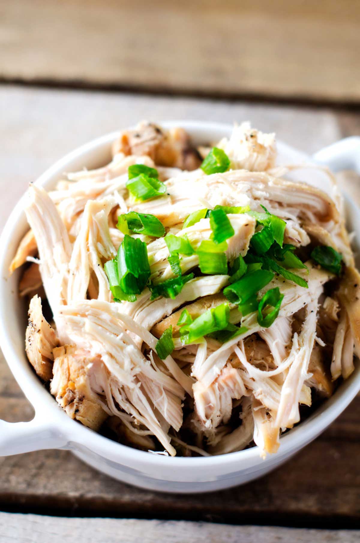 Close up photo of a white dish with slow cooker shredded chicken garnished with scallions.
