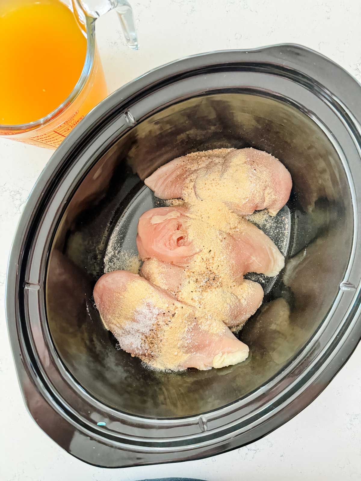 Seasonings over chicken breast in a slow cooker.