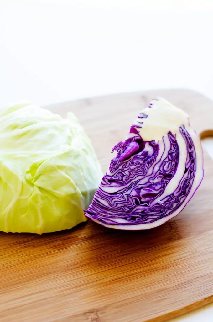 Photo of red cabbage and white cabbage on a cutting board against a white background.