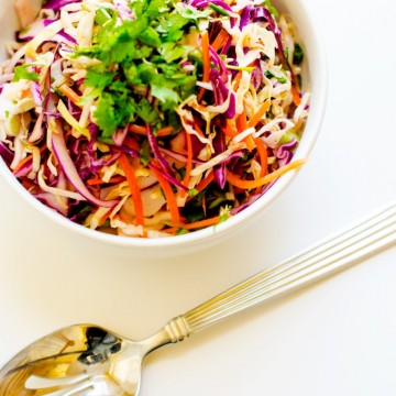 Photo of Citrus Slaw garnished with parsley in a white bowl with a serving spoon next to it on a white background.