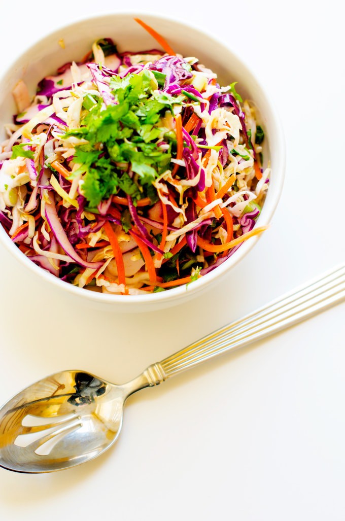 Photo of Citrus Slaw garnished with parsley in a white bowl with a serving spoon next to it on a white background.