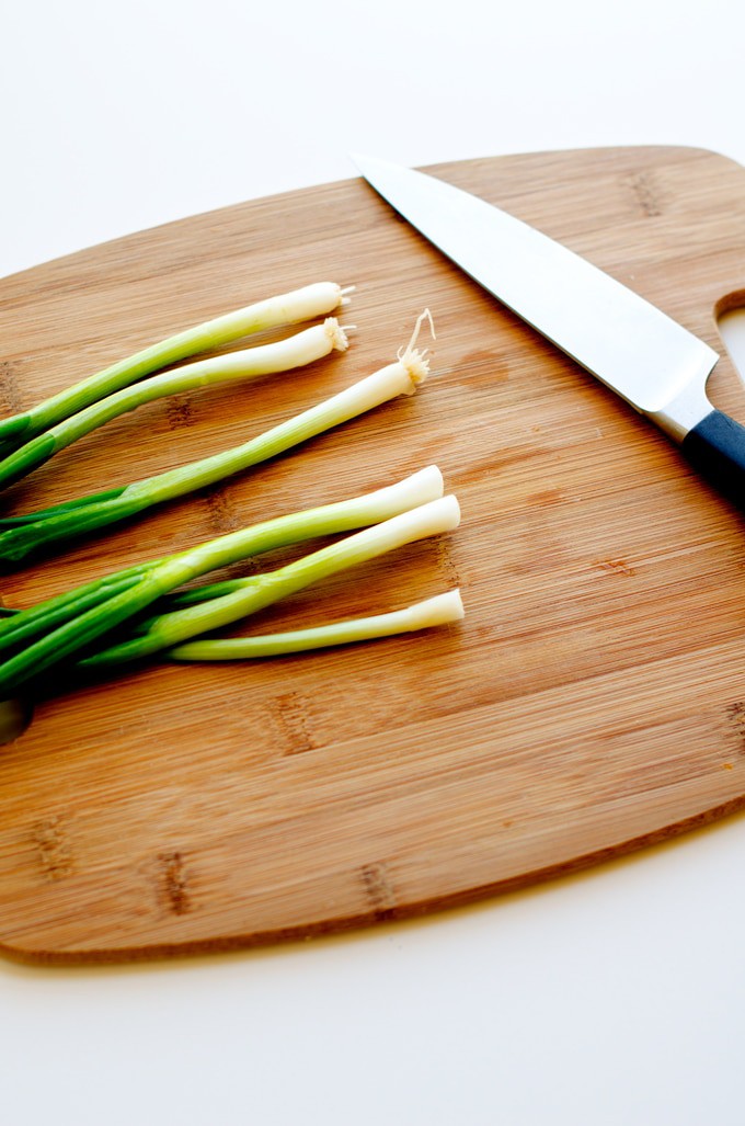 Photo of green onions and a knife on a cutting board agains a white background.