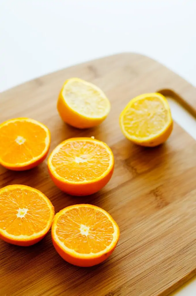 Photo of halved oranges on a wooden cutting board.