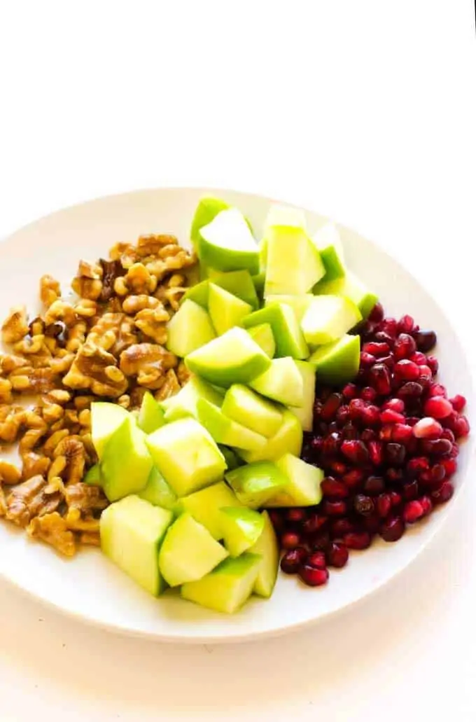 Photograph of chopped walnuts, diced apples and pomegranate ariels on a white plate.