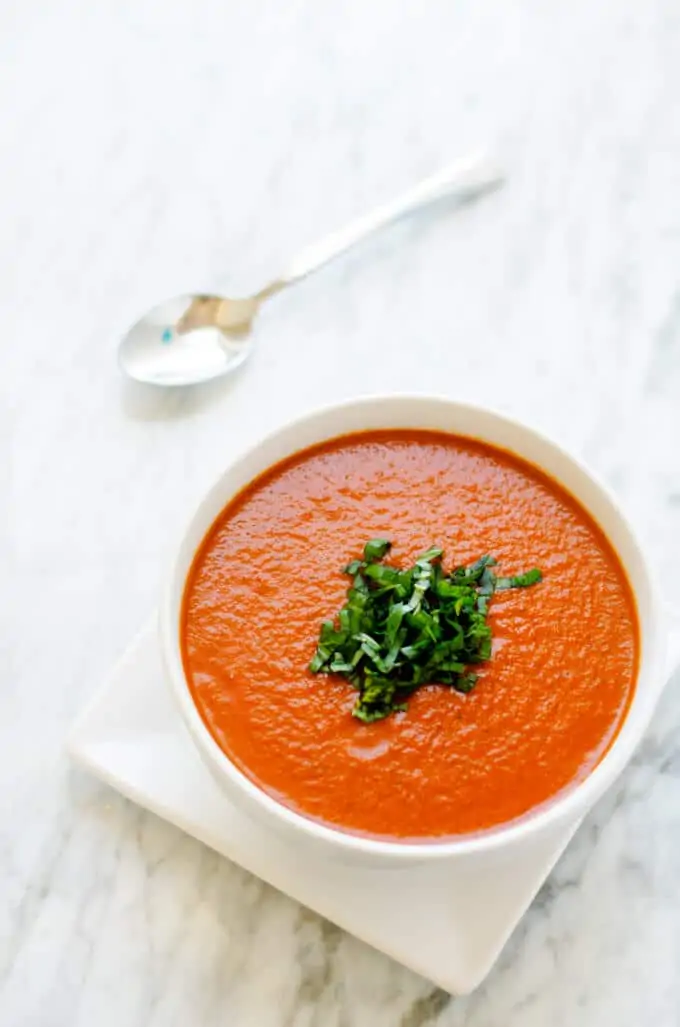 Tomato Red Pepper Soup in a white bowl on a white marble background.