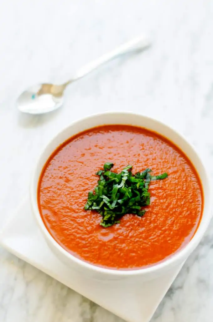 Close-up shot of Roasted Red Pepper Tomato Soup in a white bowl on a white marble background.