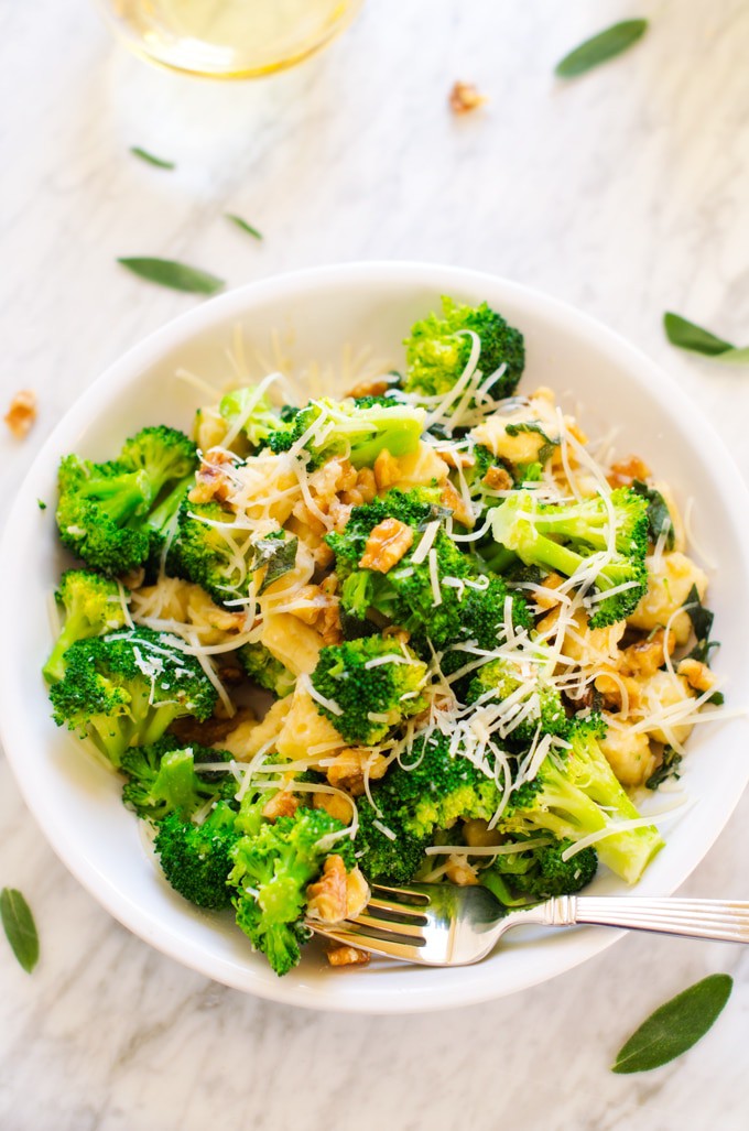 White plate with Gnocchi and Broccoli garnished with sage and walnuts.