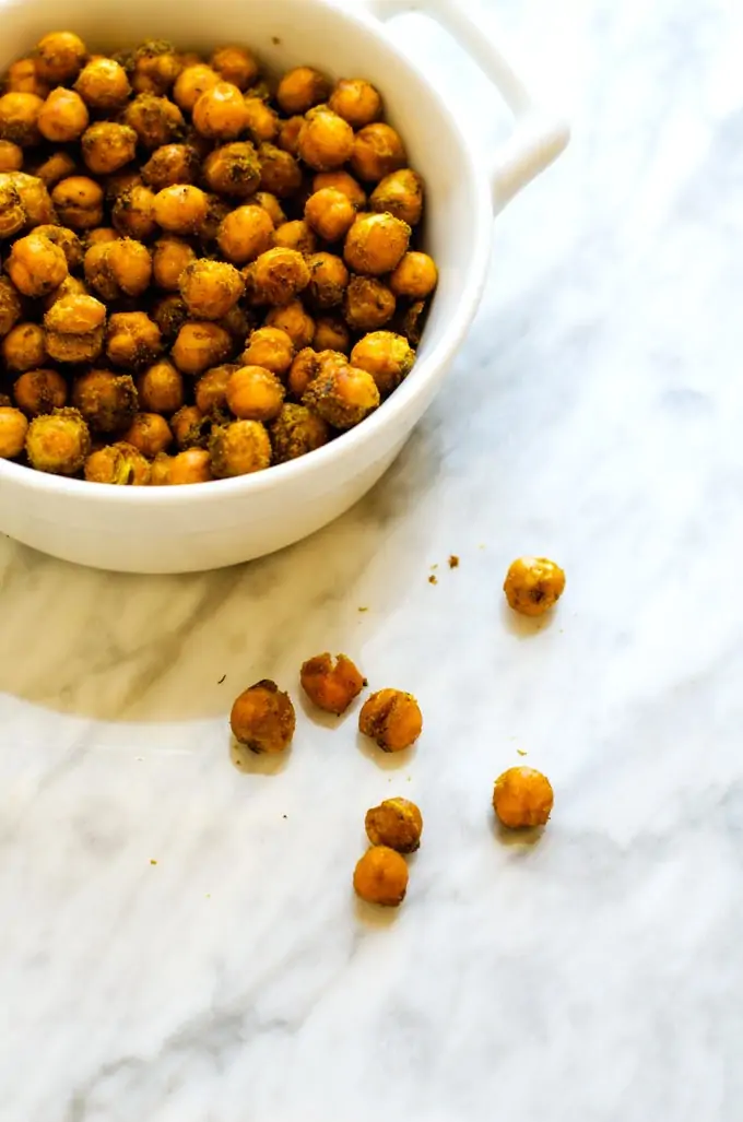 Small bowl of Curried Roasted Chickpeas with chickpeas scattered on a white background