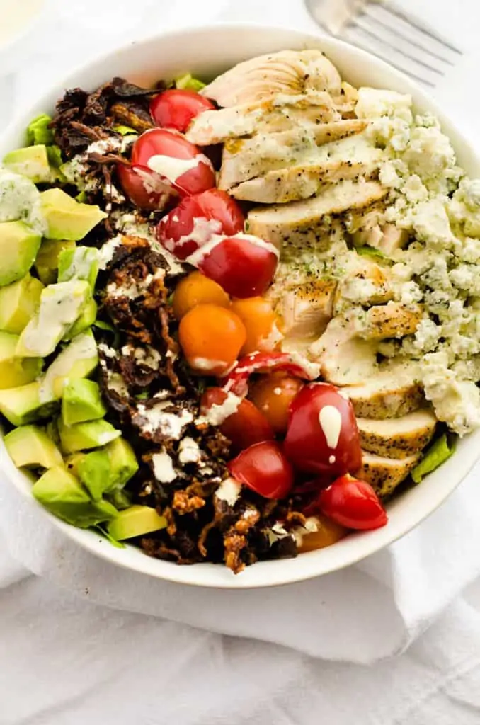 Overhead photo of a Avocado Grilled Chicken Salad in a white bowl drizzled with a creamy dressing.