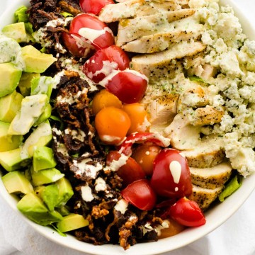 Square Overhead photo of a Avocado Grilled Chicken Salad in a white bowl drizzled with a creamy dressing.