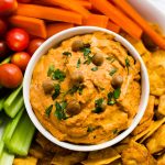 Square overhead photo of roasted red pepper hummus surrounded by fresh veggies and crackers.