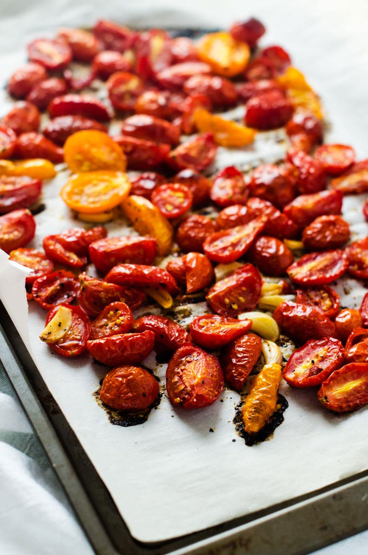 Grape tomatoes roasting on a parchment lined baking sheet.