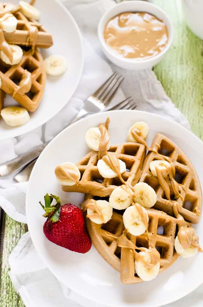 Overhead photo of Gluten Free Peanut Butter Waffles on a white plate with a small dish of maple peanut butter behind it and another plate of waffles to the left.