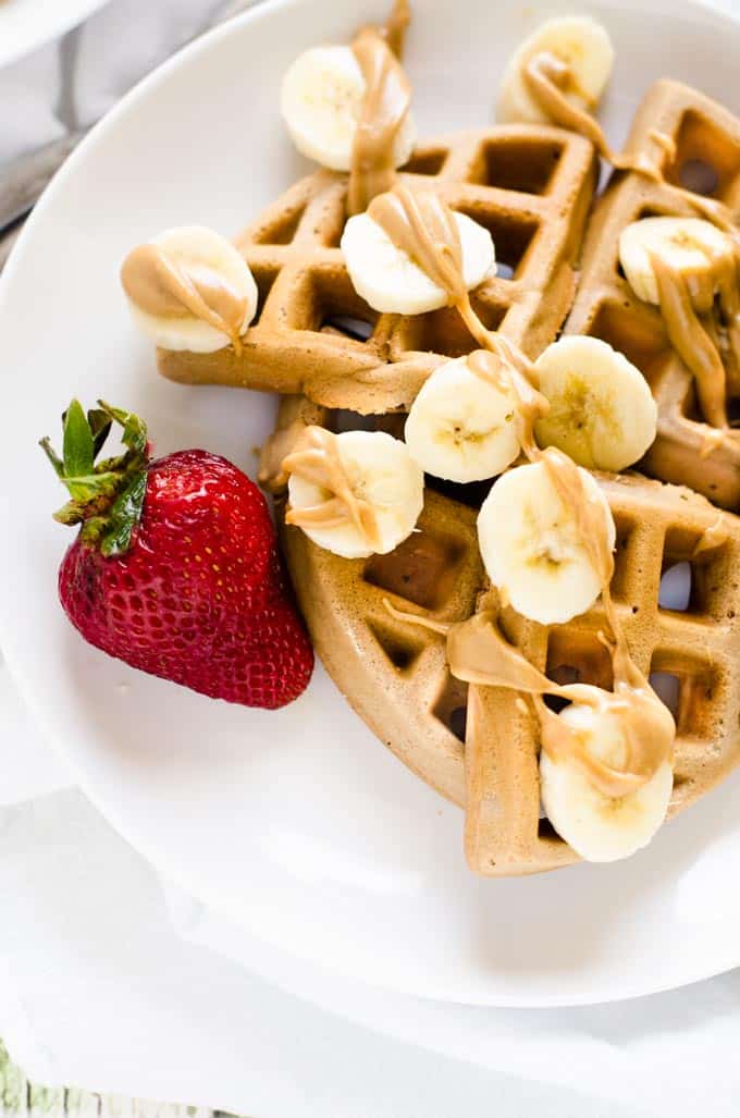 Photo of Gluten Free Peanut Butter Waffles on a white plate with bananas and peanut butter on top.