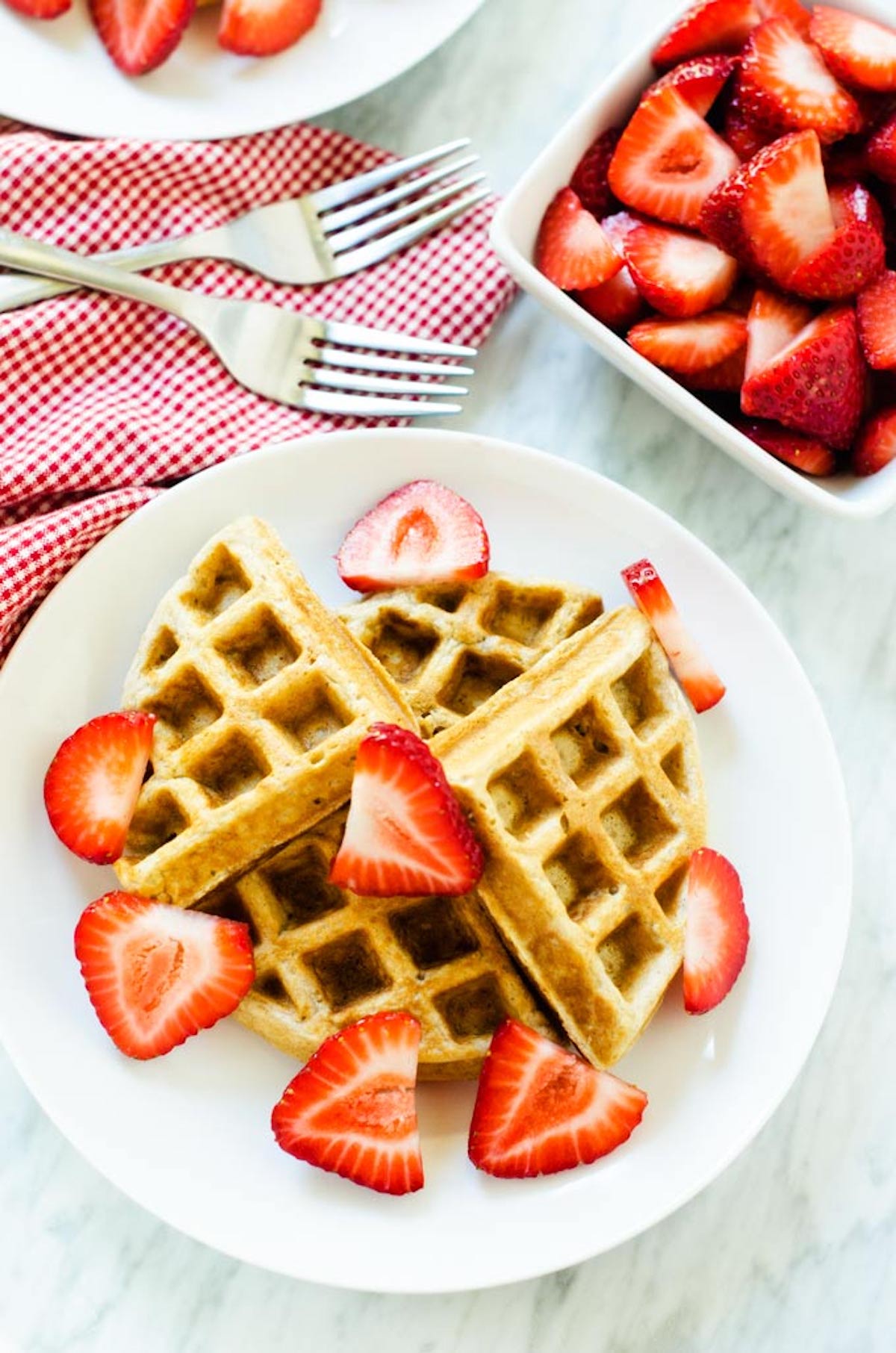 Photo of a white plate with oatmeal waffles topped with strawberries.