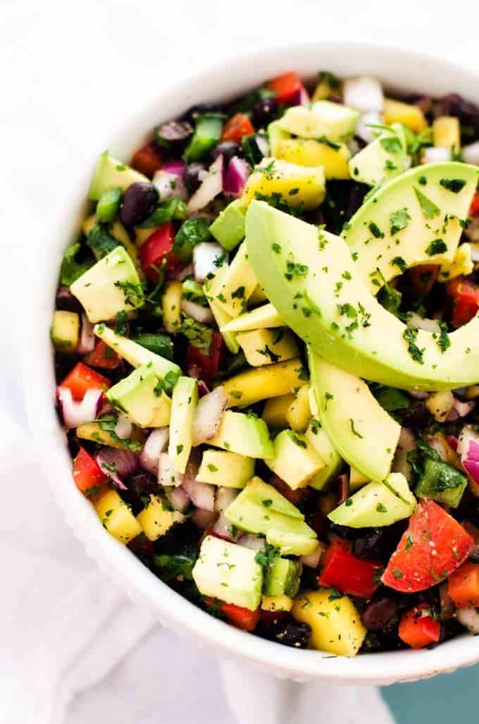 Close up photo of Mango Avocado Salsa in a white bowl garnished with parsley and avocado.