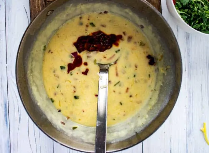 Photo of a cooked queso dip recipe with a chipotle chili pepper being added in.