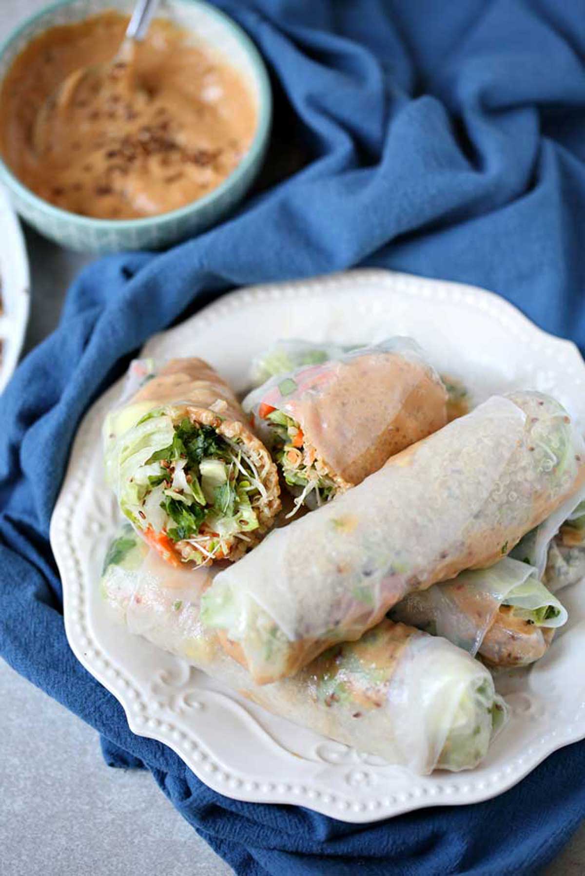 A white plate with vegan summer rolls sitting on top of a blue napkin.