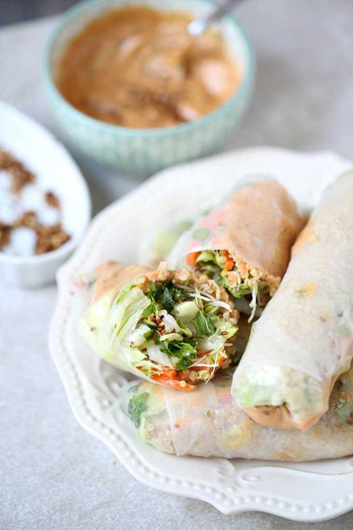 Vegan spring rolls on a white plate with peanut dipping sauce behind them.
