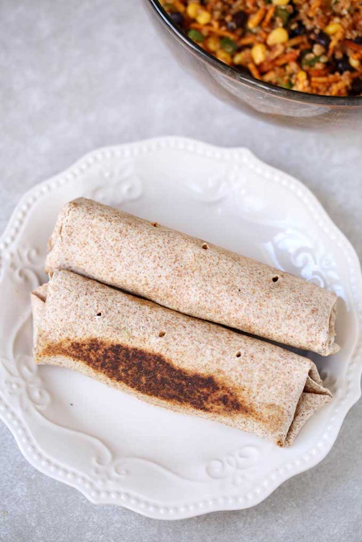 Quinoa burritos on a white plate that haven't yet been cut for serving.