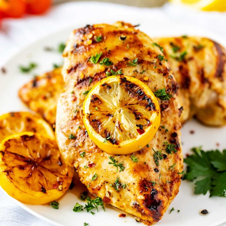 Photo of a white plate with grilled lemon pepper chicken garnished with parsley and lemons.