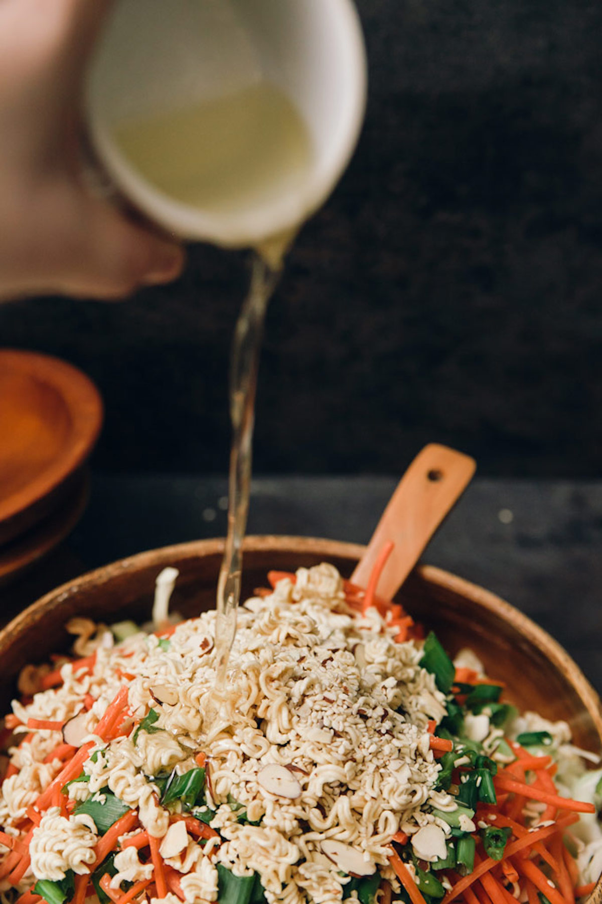 Sesame dressing being poured on top of a toasted noodle salad.
