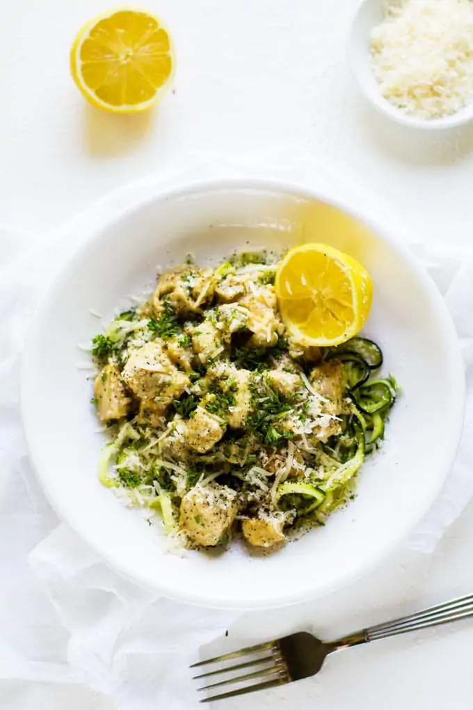 Overhead photo of Zucchini Alfredo in a white bowl on a white background with a lemon.