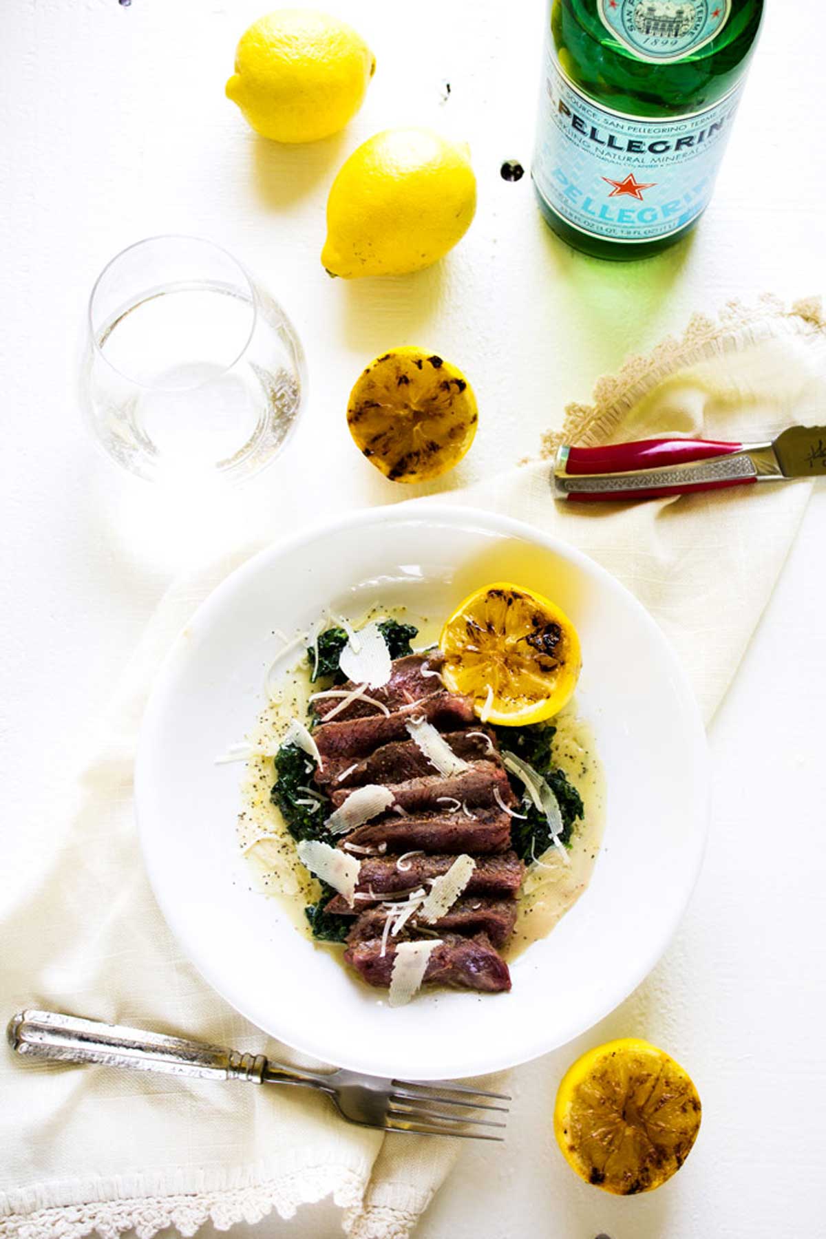 Overhead photo of steak with spinach garnished with parmesan and lemon.