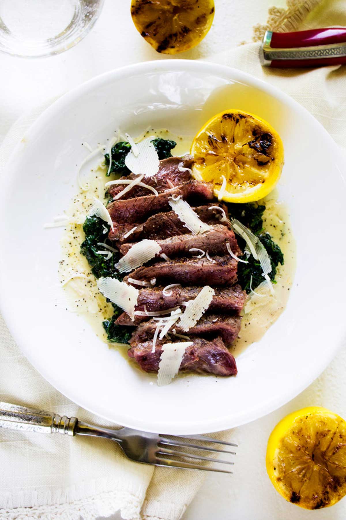 Close up overhead photo of steak with spinach in a white dish.