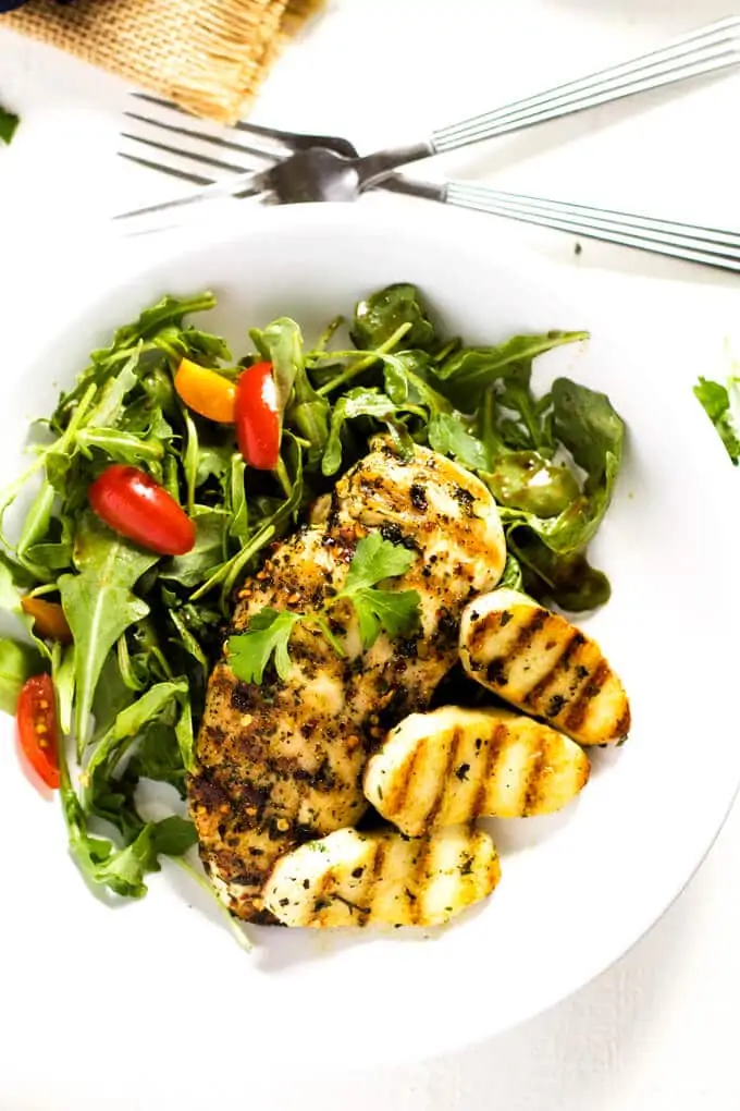 Overhead photo of a white plate with chicken and halloumi salad on a white background with two forks next to it.