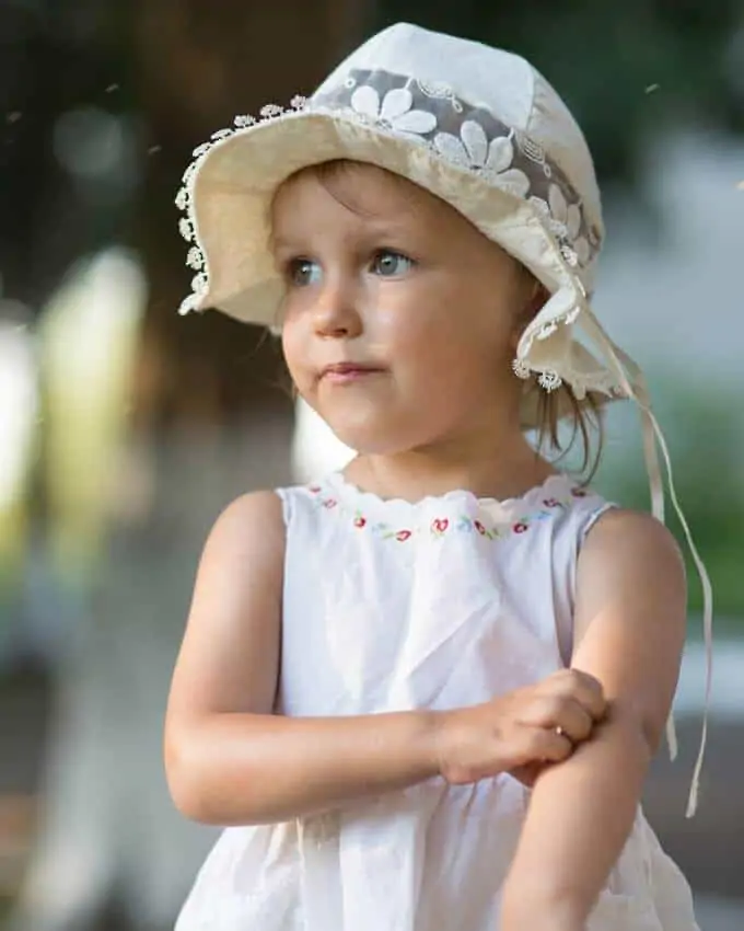 Photo of little girl in a white had scratching a bug bite - Essential Oils for Bug Bites