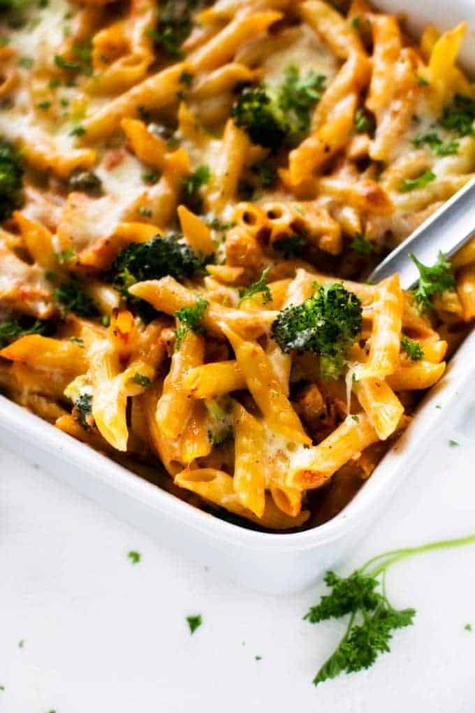 Close up photo of chicken broccoli penne pasta with marinara sauce in a white casserole dish.