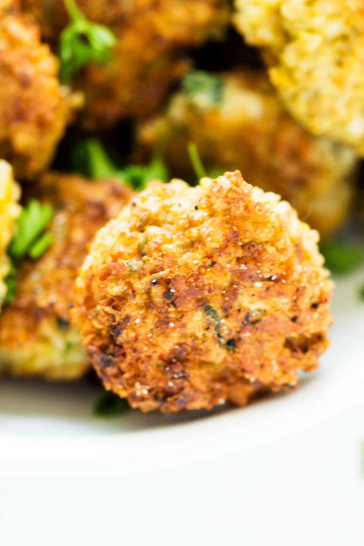 Close up photo of a quinoa fritter on a white plate with other quinoa fritters behind it.