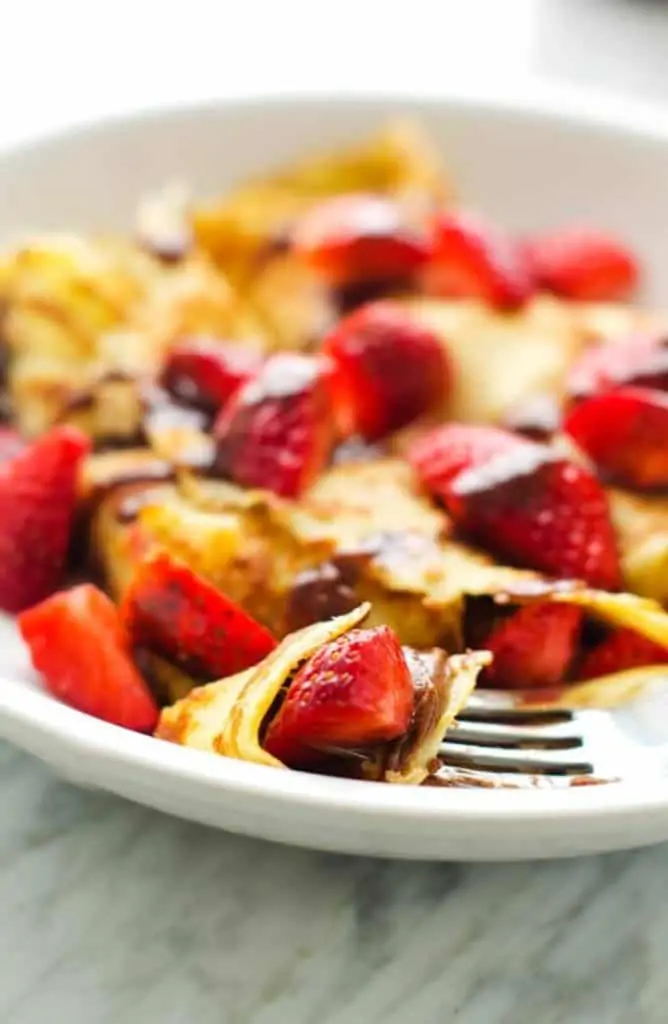 Photo of a fork full of gluten free crepes topped with strawberries and chocolate sauce.