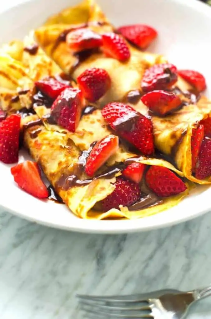 Side photo of gluten free crepes drizzled with chocolate hazelnut sauce topped with strawberries.