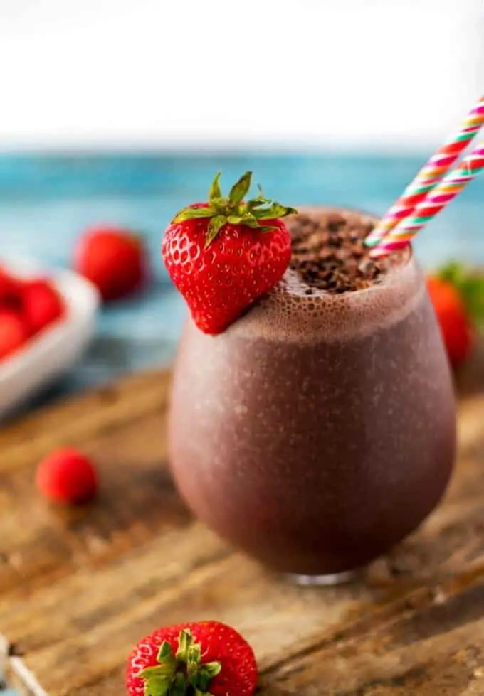 Side photo of Acai smoothie with two straws garnished with cacao nibs and a strawberry.