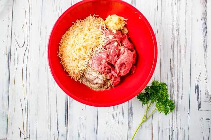 Ground beef, cheese, garlic, and seasonings in a red bowl.