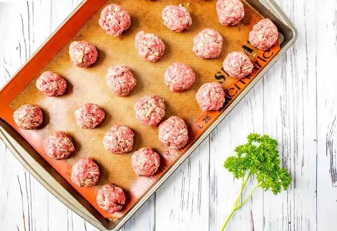 Baking sheet of meatballs made out on a lined baking sheet.