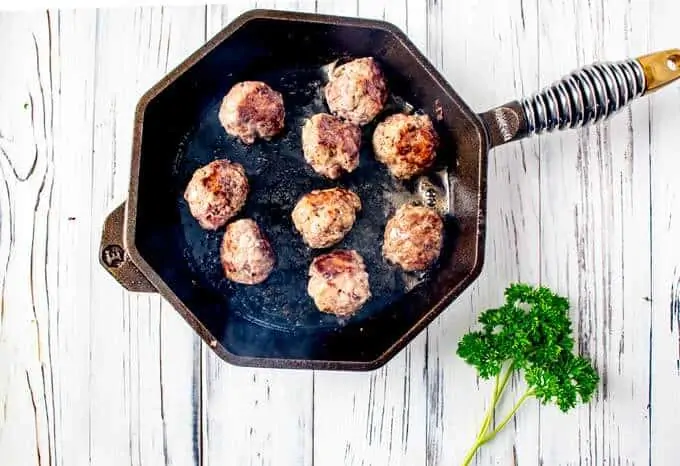 Meatballs being browned in a cast iron skillet.