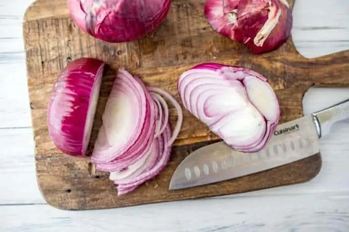 Photo of a red onion being cut on a dark cutting board for quick pickled onions.