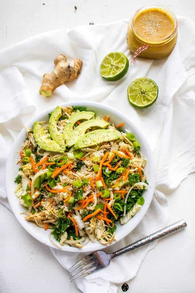 Overhead photo of Asian Chicken Salad with fresh lime and ginger and a jar of Asian Salad Dressing sprinkled with sesame seeds