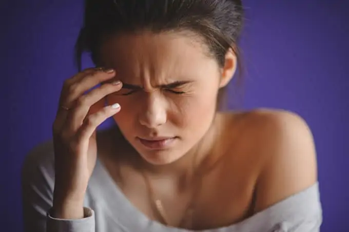 Photo of a woman clutching one side of her head with a headache.