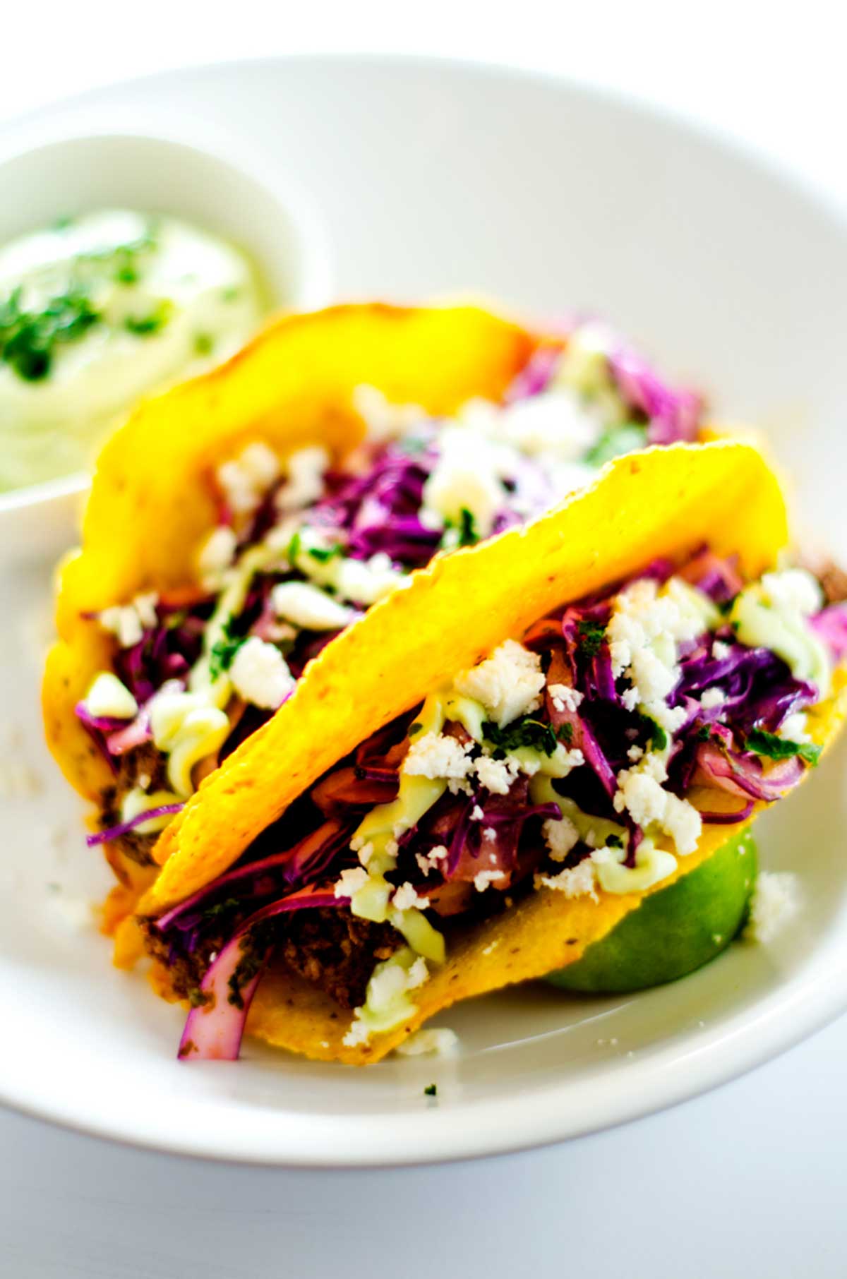 Close up photo of two beef tacos with cilantro slaw on a white plate.