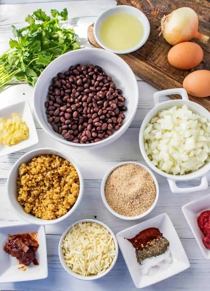 Photo of black beans, onion, breadcrumbs, quinoa, spices, cheese, tomato paste, garlic, and chipotle chili pepper in small prep bowls.