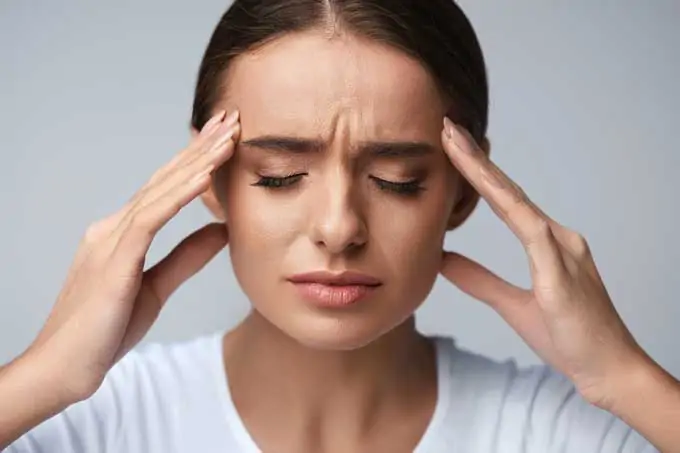 Photo of a women with a tension headache clutching both sides of her head.