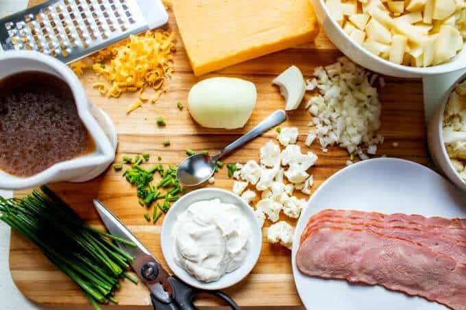 Photo of cheese being grated and vegetables being chopped with a dish of sour cream and a plate of bacon next to it.