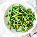 Square overhead photo of a white plate with green beans with bacon.
