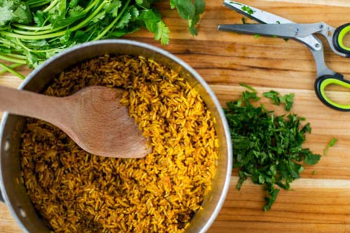 Pot with Turmeric Rice in it sitting on a cutting board with cilantro around it.