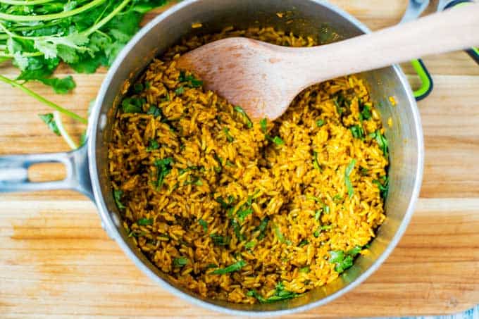Pot of Turmeric Rice with cilantro being stirred in.