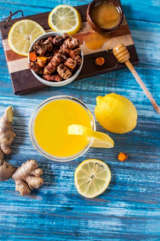 Photo of Ginger Turmeric Tea in a glass garnished with lemon and surrounded by fresh lemon, turmeric and ginger